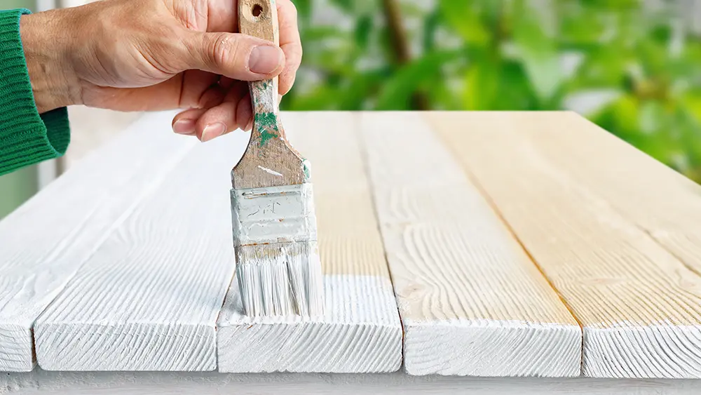 Homem pintando móvel com tinta branca para madeira.