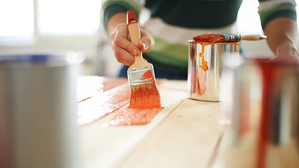 Mulher pintando móvel com laca colorida.